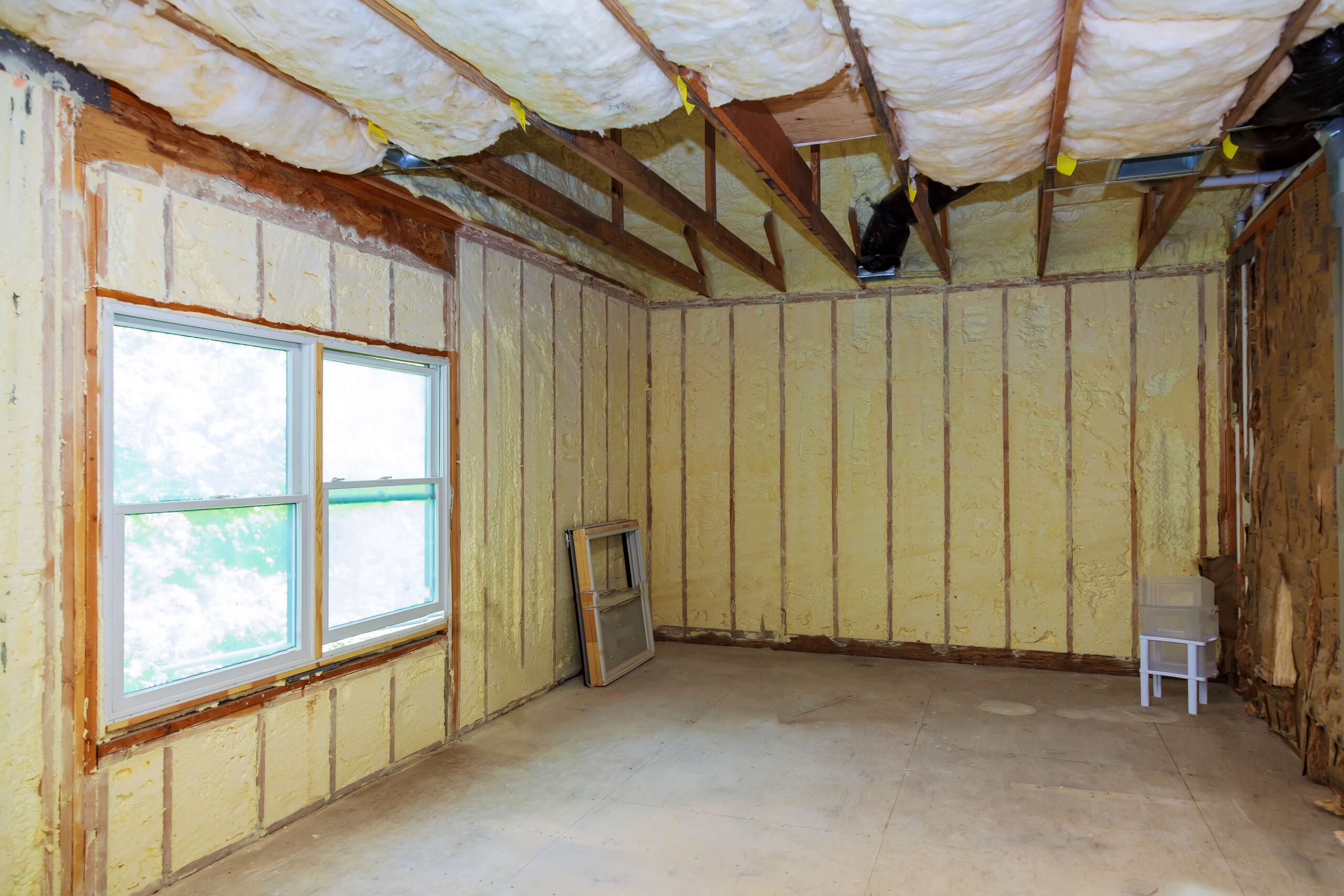 Room under renovation with exposed Pink Elephant Insulation on walls and ceiling, a double window on the left, and a small chair in the corner.